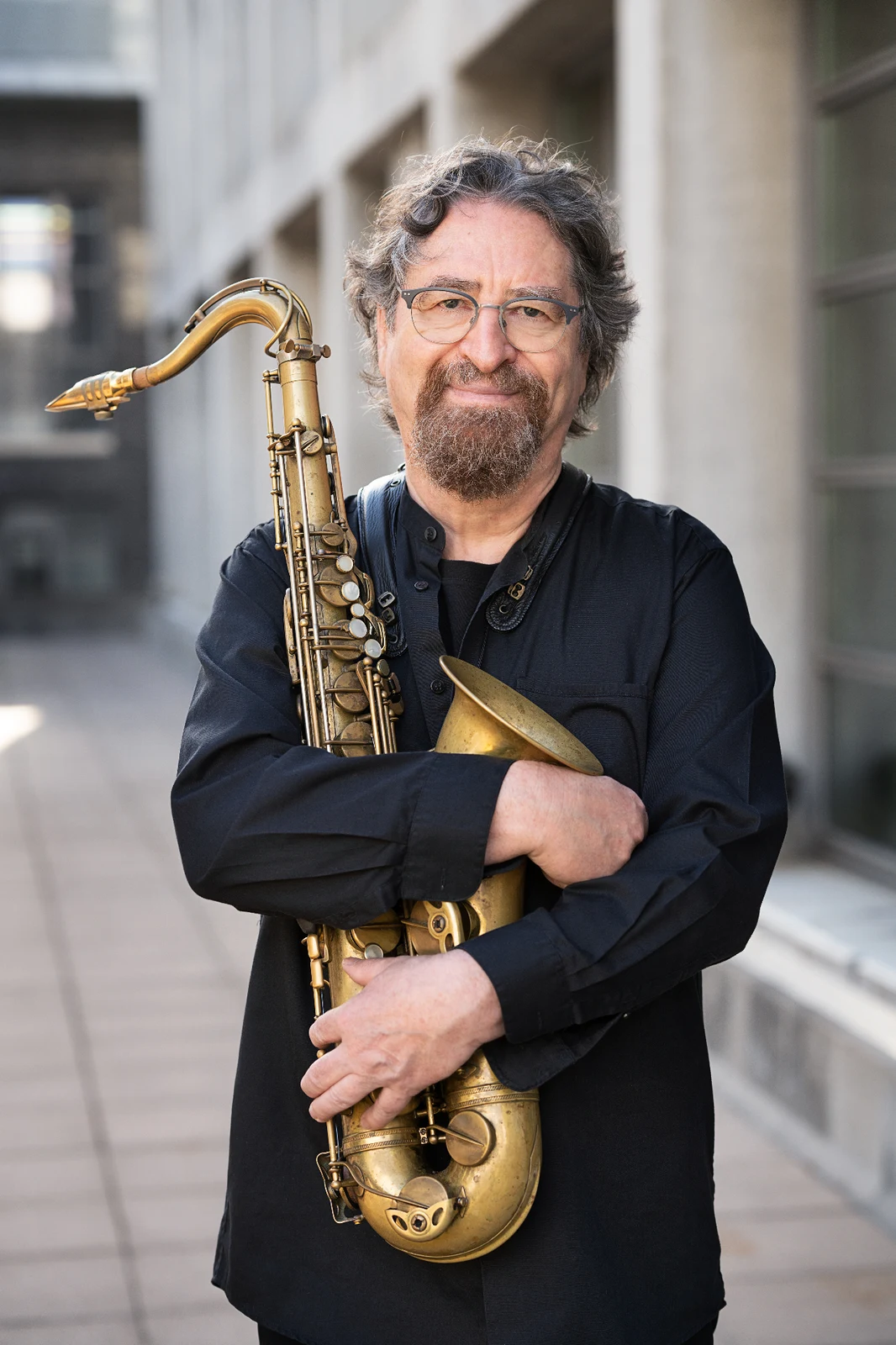 Daniel Guggenheim holding his tenor saxophone, outdoor portrait in front of modern architecture — Photo: Anja Jahn